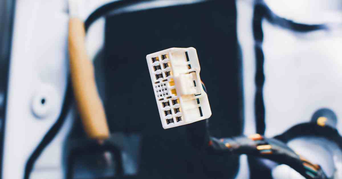 A white, rectangular automotive connector has 18 sockets for wires to connect a vehicle&rsquo;s electric system.