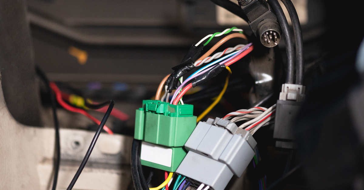 A large green and a gray, rectangular automotive connectors in a vehicle with various wires connected to each one.