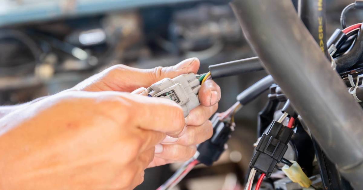 A pair of hands attaches two connectors to a large engine block. Some other black connectors are also in the background.