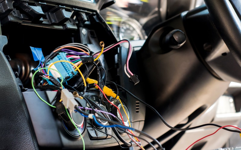The internal wiring of a car's electrical system. Several colorful wires and connectors are coming out through the radio dash.