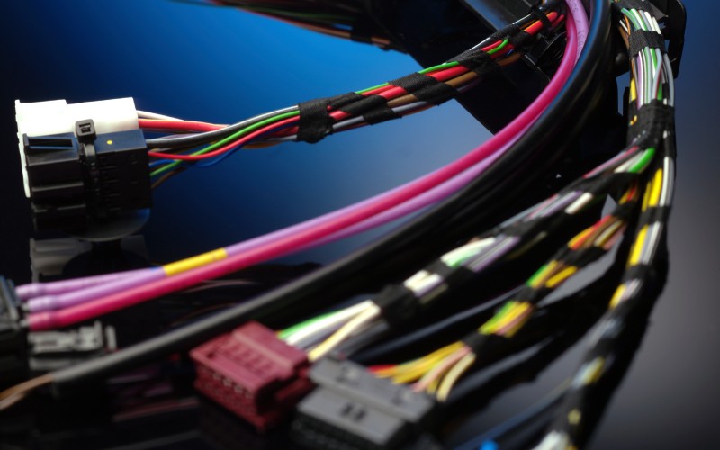 Several colorful wires are bundled together with electrical tape and shaped into a curve. At the end of these wires are many vehicle connectors.