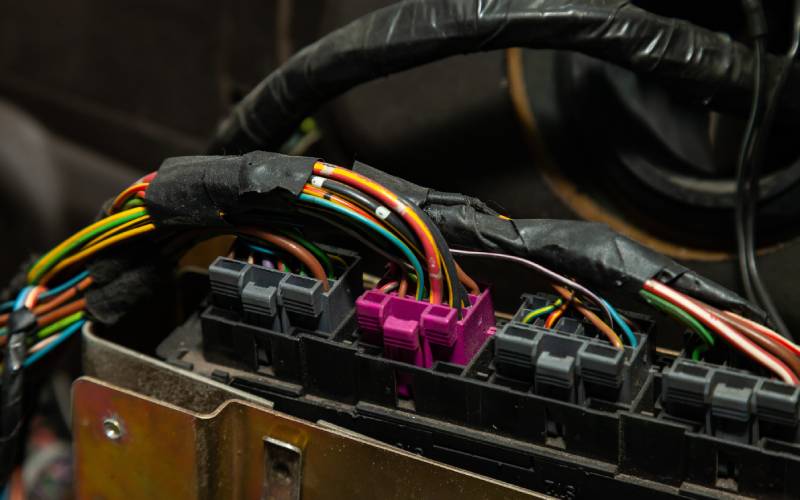 Several wrapped up wires connect to automotive connectors. Many colorful wires are going into a bright purple connector.