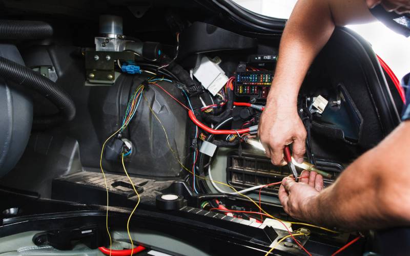 A close-up of someone using a tool to work with multi-colored wires inside a car&rsquo;s electrical system.