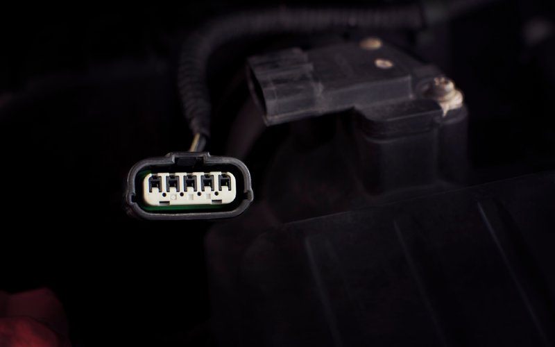 A close-up of a black 5-cavity connector with a shallow depth of field. The background is blurry and dark.