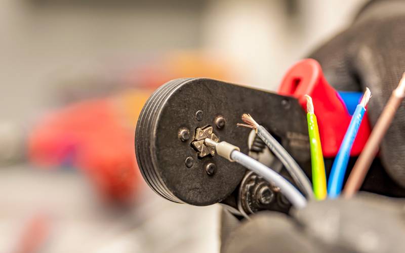 A close-up of someone holding five different-colored wires up to a crimping tool. A silver wire is in the tool being crimped.