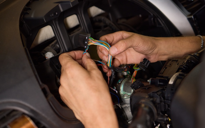 A close-up of a person separating the colorful wires that are connected to a vehicle&rsquo;s electrical system.