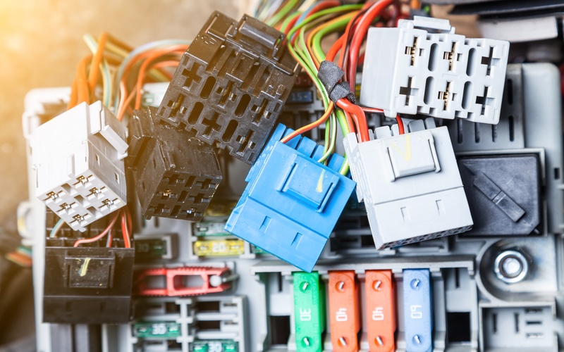 A close-up of a pile of white, blue, and black automotive connectors with an array of colorful wires attached to them.