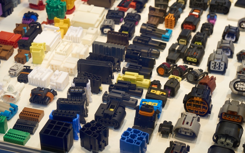 Many plastic automotive electrical connectors of different colors and sizes arranged neatly on a white surface.