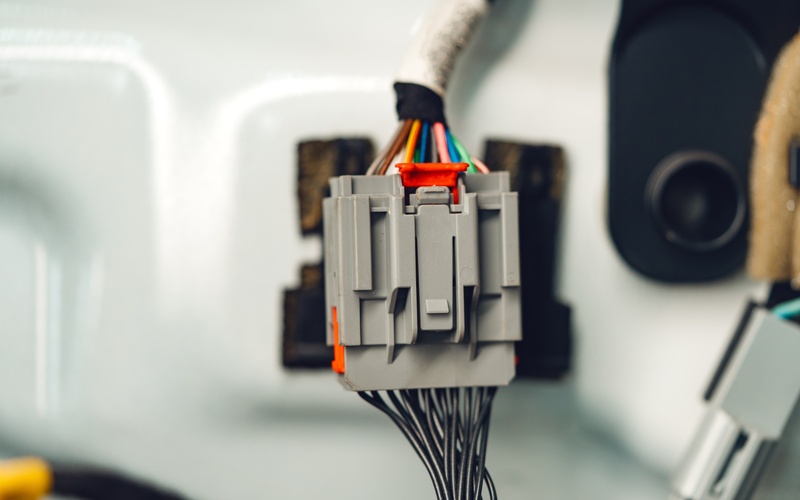 A gray plastic connector with colorful wires coming out of it on one side and black wires coming out of the other.