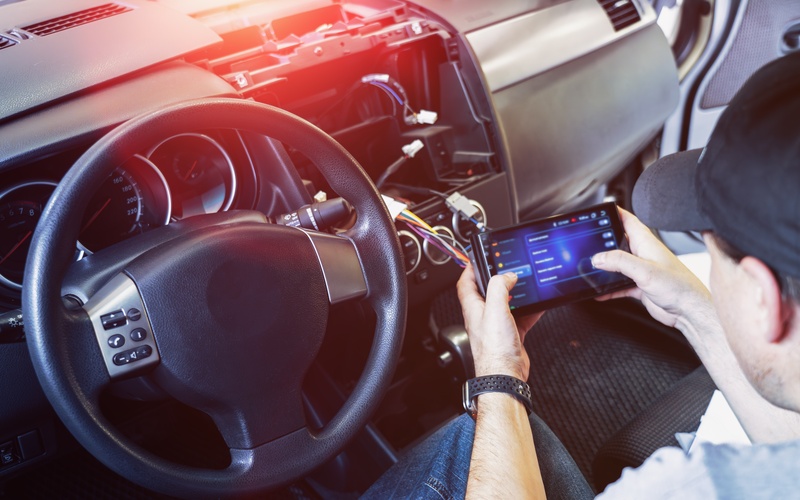 A man holds a new car radio with a touch screen in his hands. It is connected to the car&rsquo;s electrical system with colorful wires.