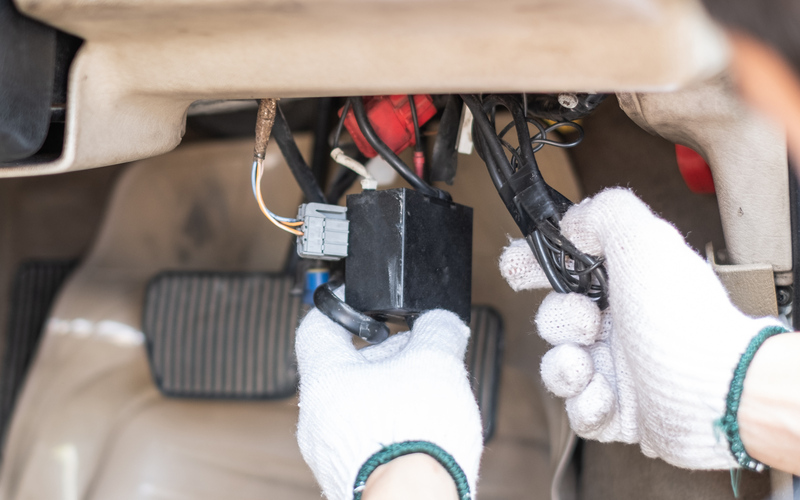A pair of hands wearing white work gloves hold wires from a car's electrical system.