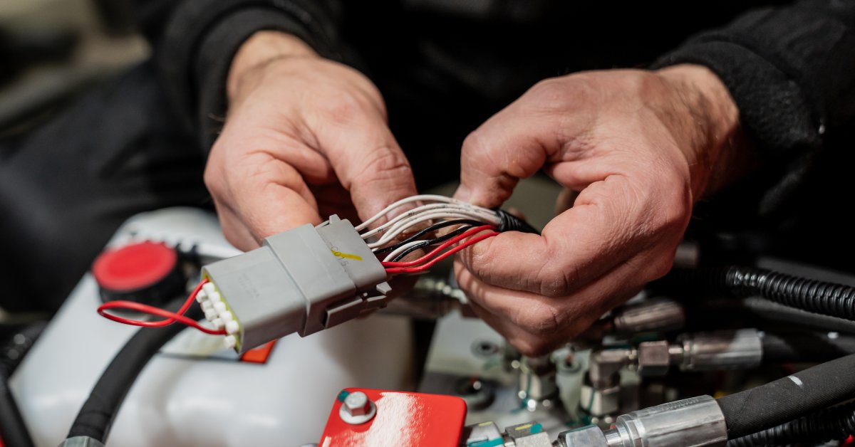 A pair of bare hands separates white, black, and red automotive wires bundled with a gray connector.