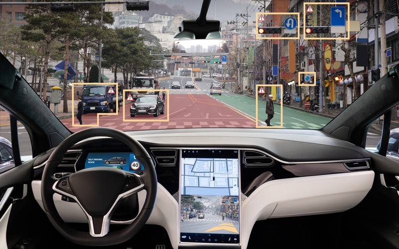 The point-of-view of a passenger in an autonomous car with a heads-up display and a black and white steering wheel.