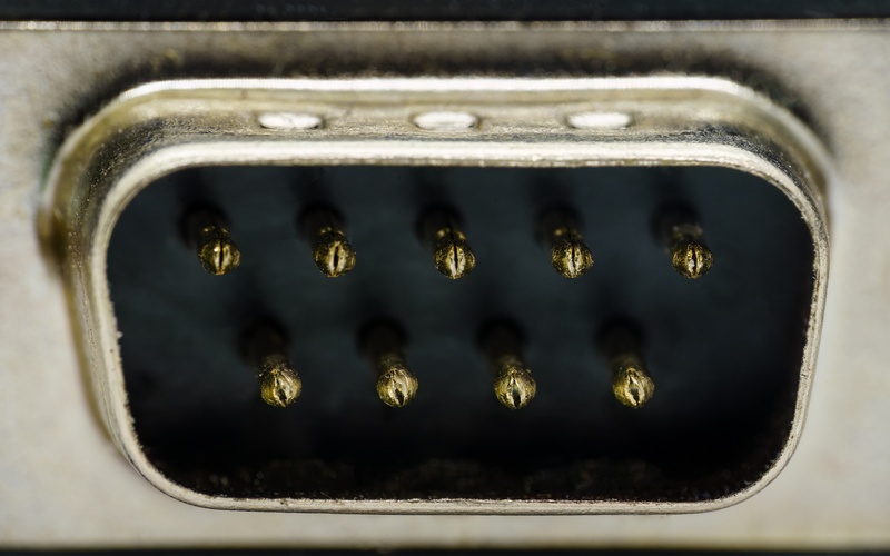 A metal automotive connector with a 9-pin outlet. The pins are shiny and are positioned in a dark cavity.