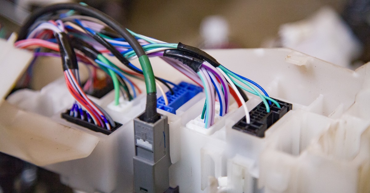 Many thin, multicolored wires are taped together with black tape and inserted into electrical connectors.