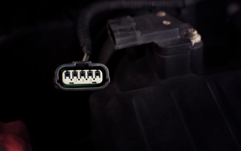 A close-up of a black 5-pin automotive wire connector with white ports in a vehicle&rsquo;s electrical system.