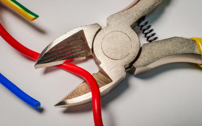 A pair of wire cutters with an uncut red wire lying across the blades. A blue wire and a yellow-and-green wire lay cut next to them.
