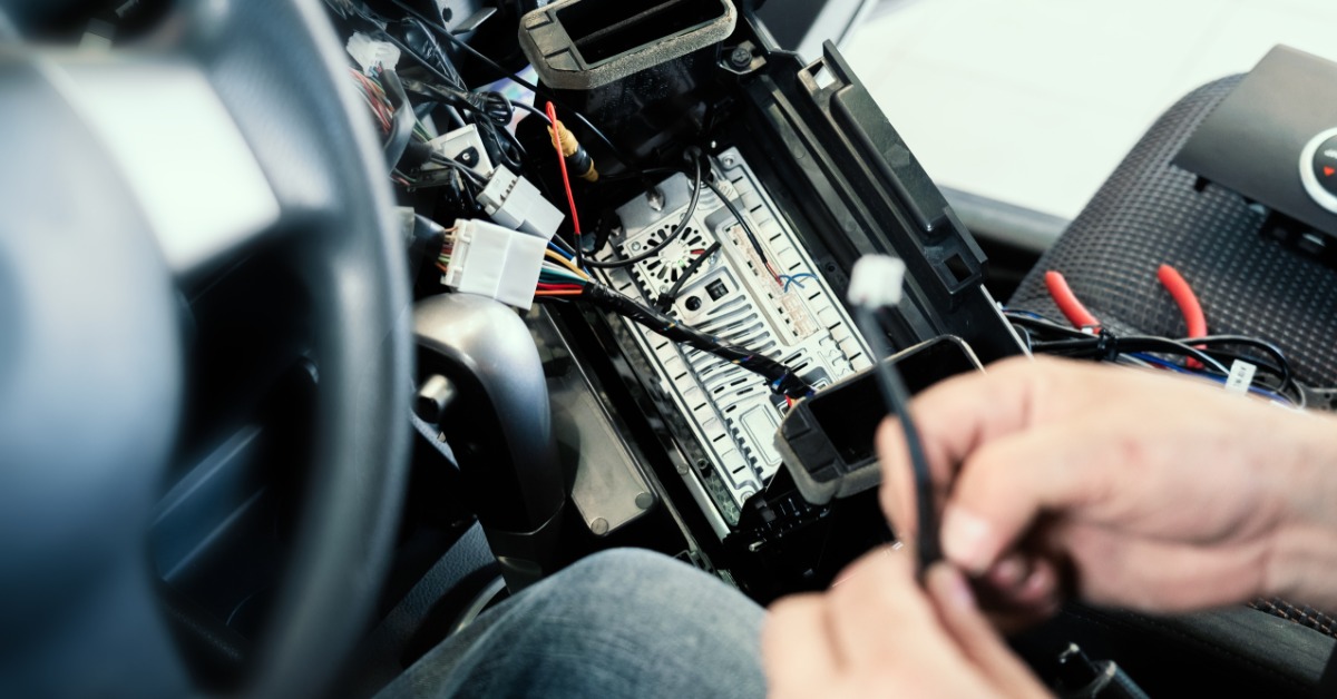 A person using their bare hands to work on connectors inside a car. The person is sitting in the driver&rsquo;s seat.