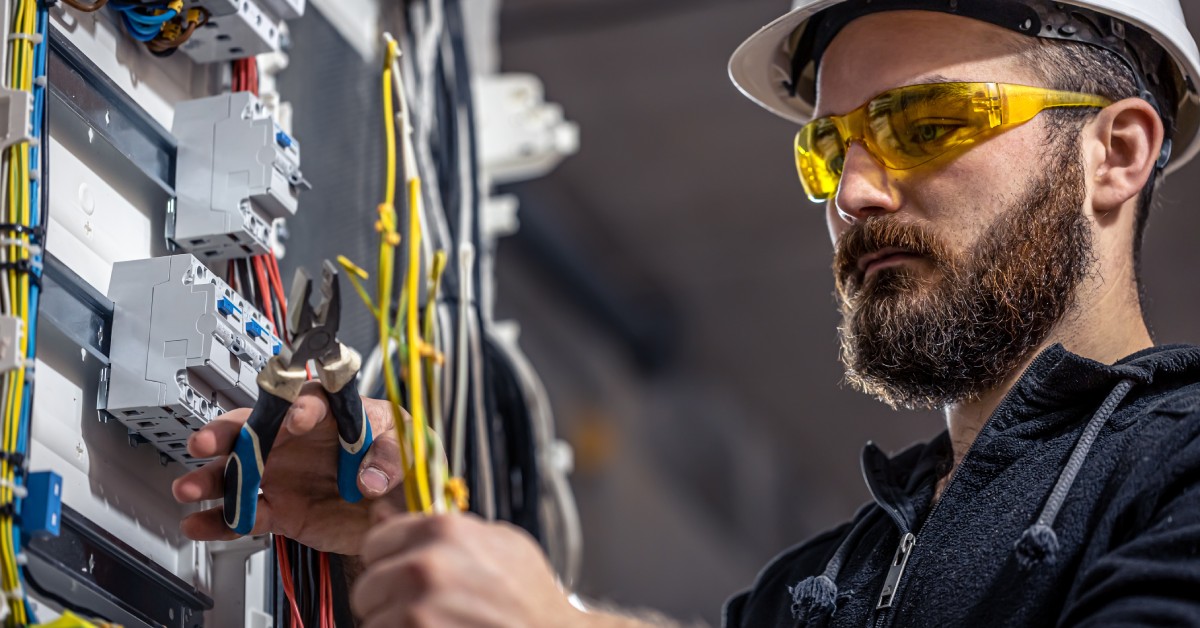 An electrician holding a small hand tool in front of a wall. The wall is covered in cables and electronics.