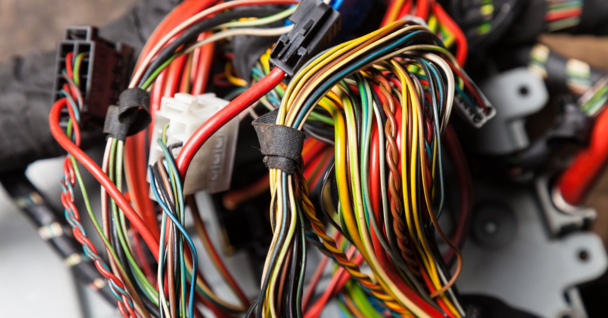 A large bundle of colorful wires attached to automotive electrical connectors. A bright light shines on the wires.