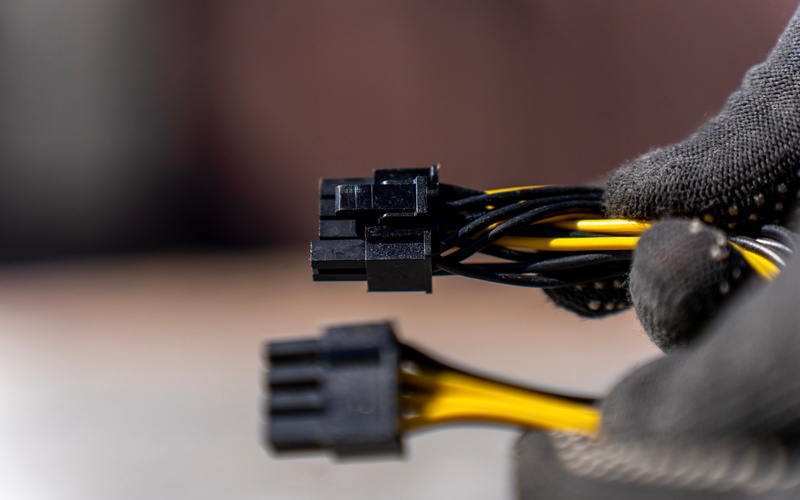 A person wearing black gloves holding two black automotive connectors with yellow wires attached to them.