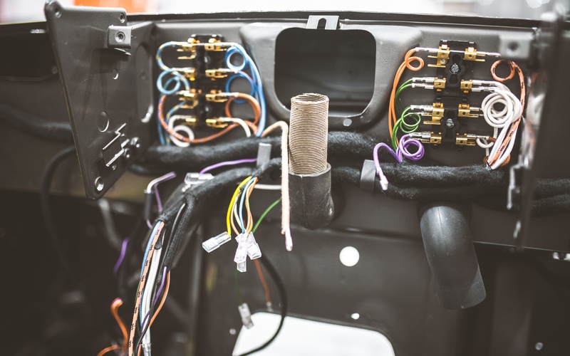 A car with its dashboard removed parked in a brightly lit shop. The wiring harness is exposed inside the car.