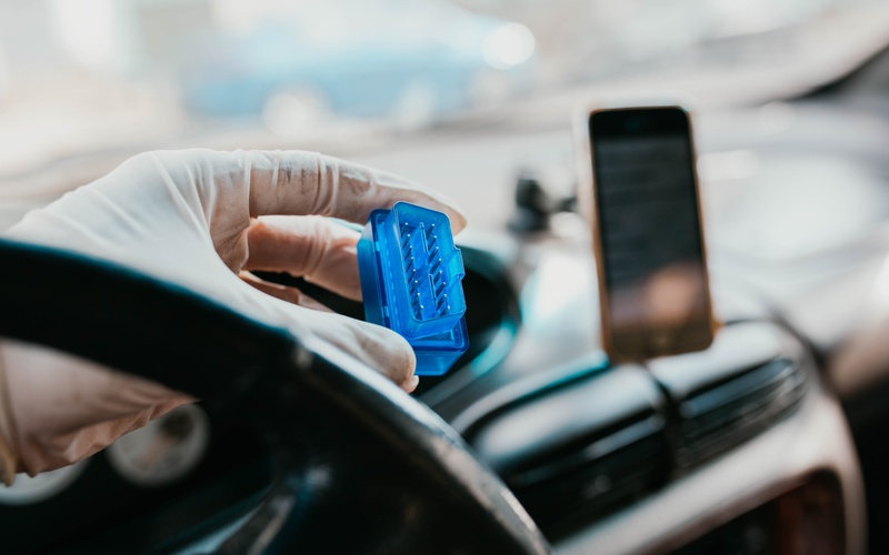 A person wearing a white glove holding a blue automotive connector in front of a car&rsquo;s interior dashboard.