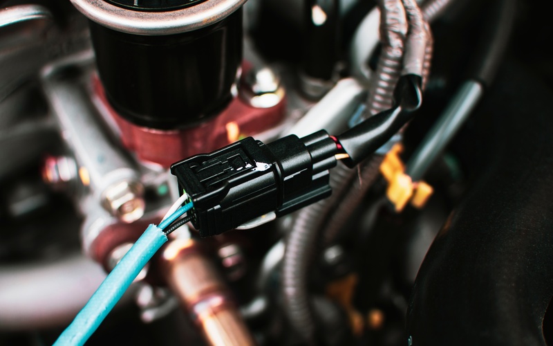 A green wire and black wire connected inside of a vehicle engine. Both wires are attached by black connectors.