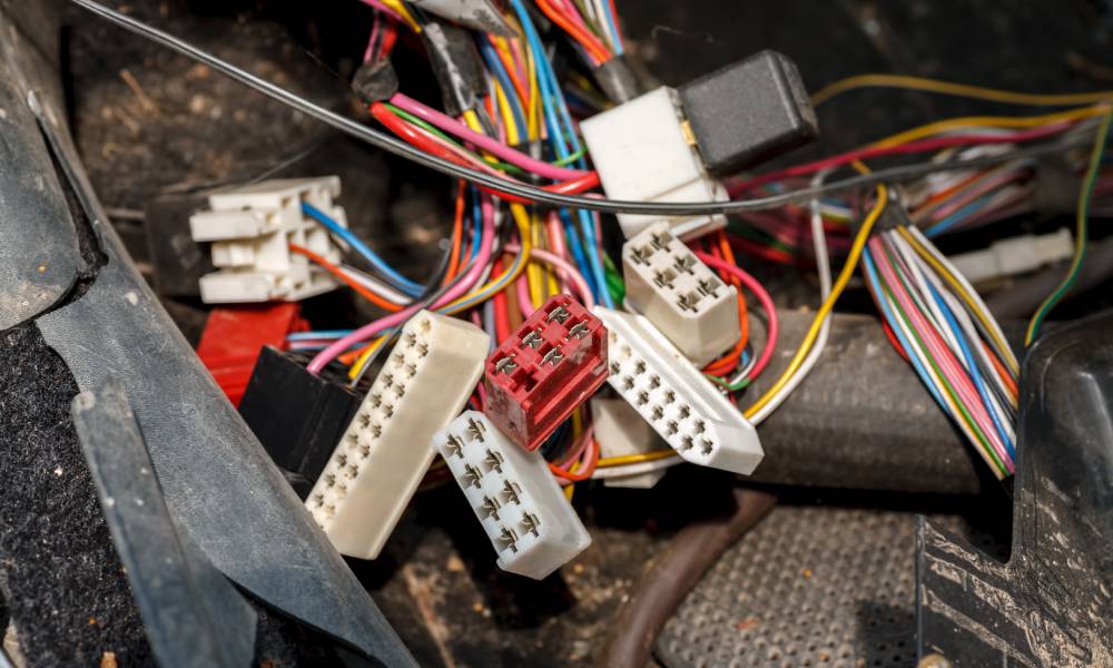 Several red, white, and black square and rectangular automotive connectors with multiple terminals inside a vehicle.